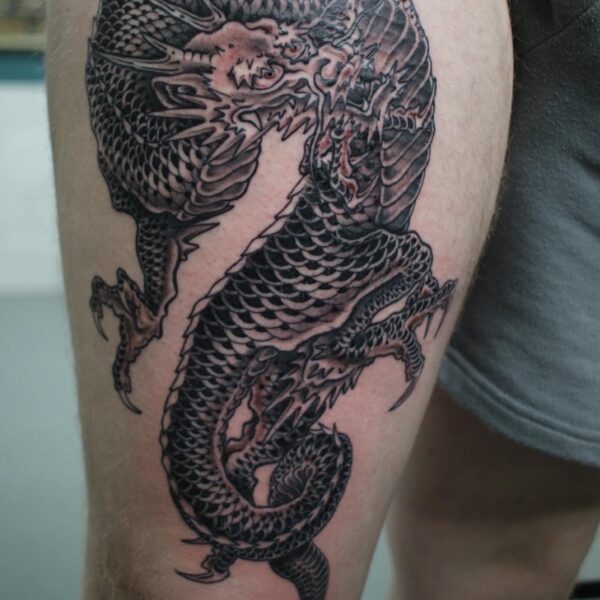Man's thigh featuring a black and grey, illustrative Dragon