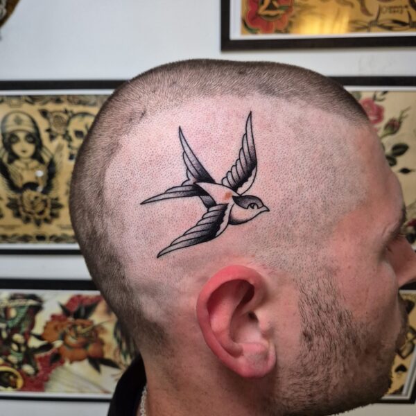 Traditional swallow tattoo on a customers temple, done by Edoardo Cucchelli. From Rome, Edoardo Cucchelli is a tattoo artist with 12 years experience. Now based at Nowhere Tattoo Shop, in Brighton, Edoardo creates tattoo's in his signature bold, rich, and detailed works.